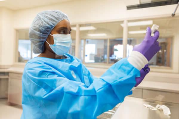 全球最大的博彩平台. Dunn 药学院 student in blue scrubs, gloves, cap and mask, holding a vial.