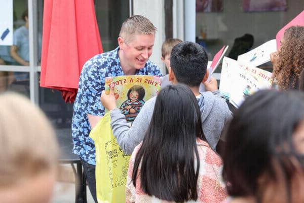 十大正规博彩网站评级博彩平台推荐大学 Children's Literature Conference speaker John Schu signs books for schoolchildren at a Rally for Reading to kick off the virtual/in-person conference in April.